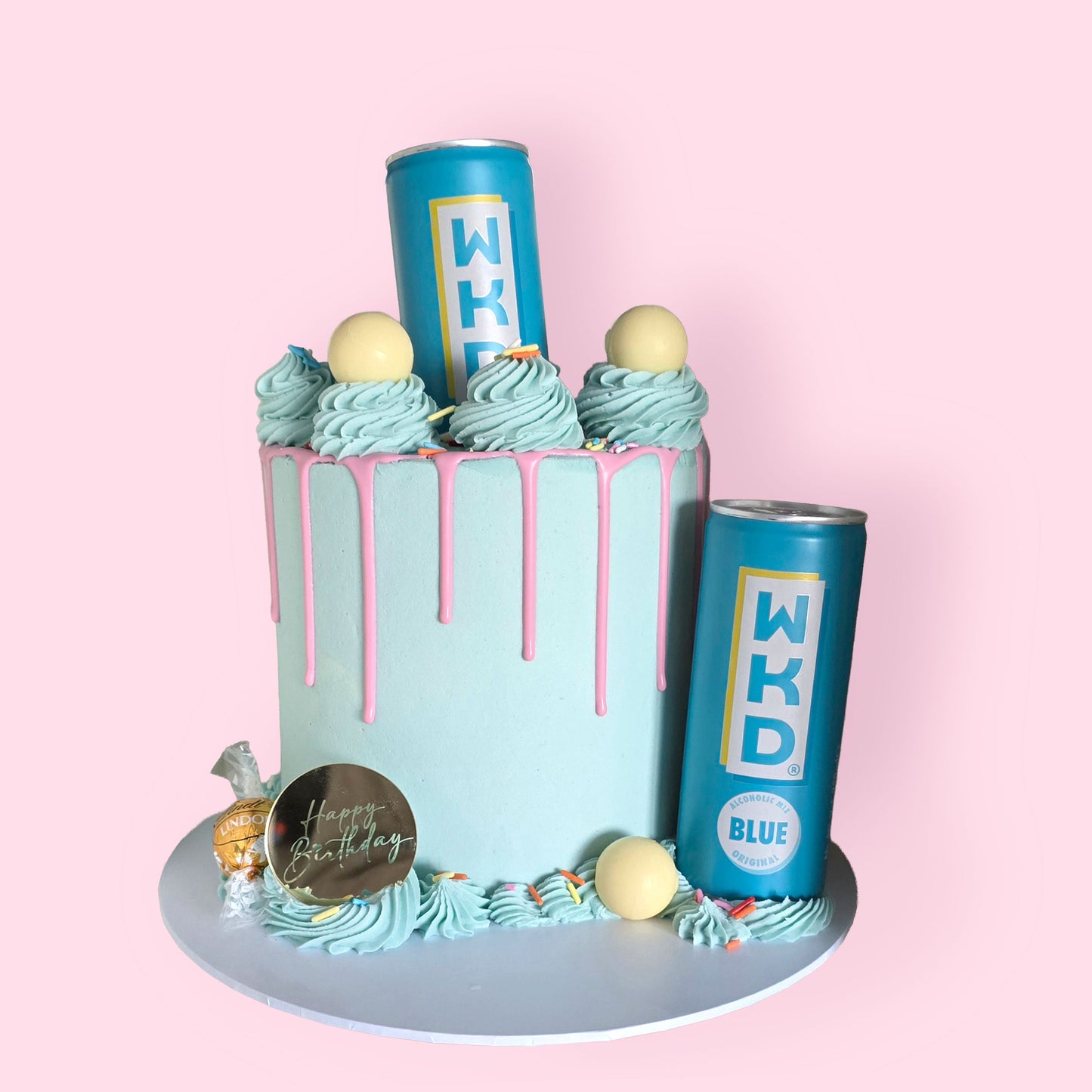 Blue birthday drip cake with pink icing, WKD Blue cans, Lindor chocolate, and pastel swirl decoration