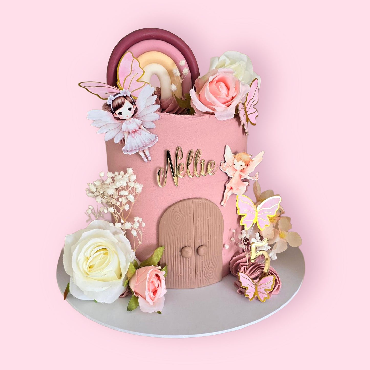 Custom fairy-themed birthday cake with pink decor, floral details, rainbow topper, and personalised name