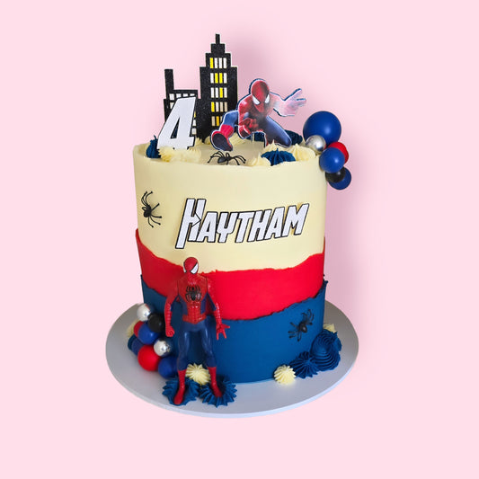 Spiderman-themed birthday cake with red, blue, and cream layers, cityscape topper, and personalised name Haytham for 4th birthday