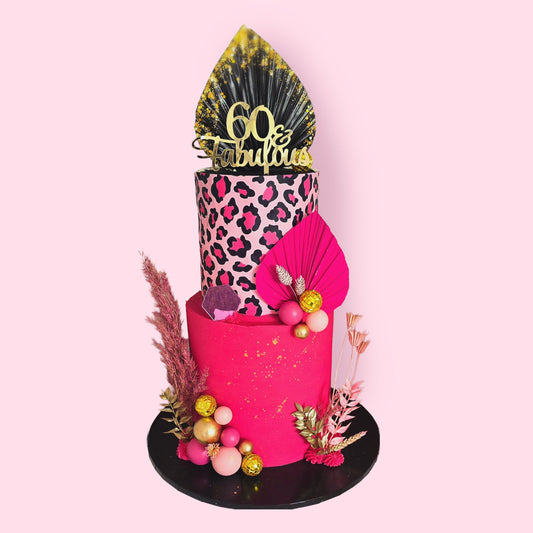 Two-tier hot pink and leopard print celebration cake with dried flowers, gold accents, and “60 & Fabulous” topper
