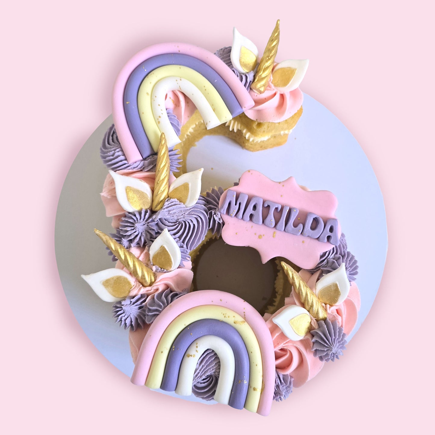 Unicorn-themed number 6 birthday cake with rainbows, gold horns, pastel buttercream, and name “Matilda”