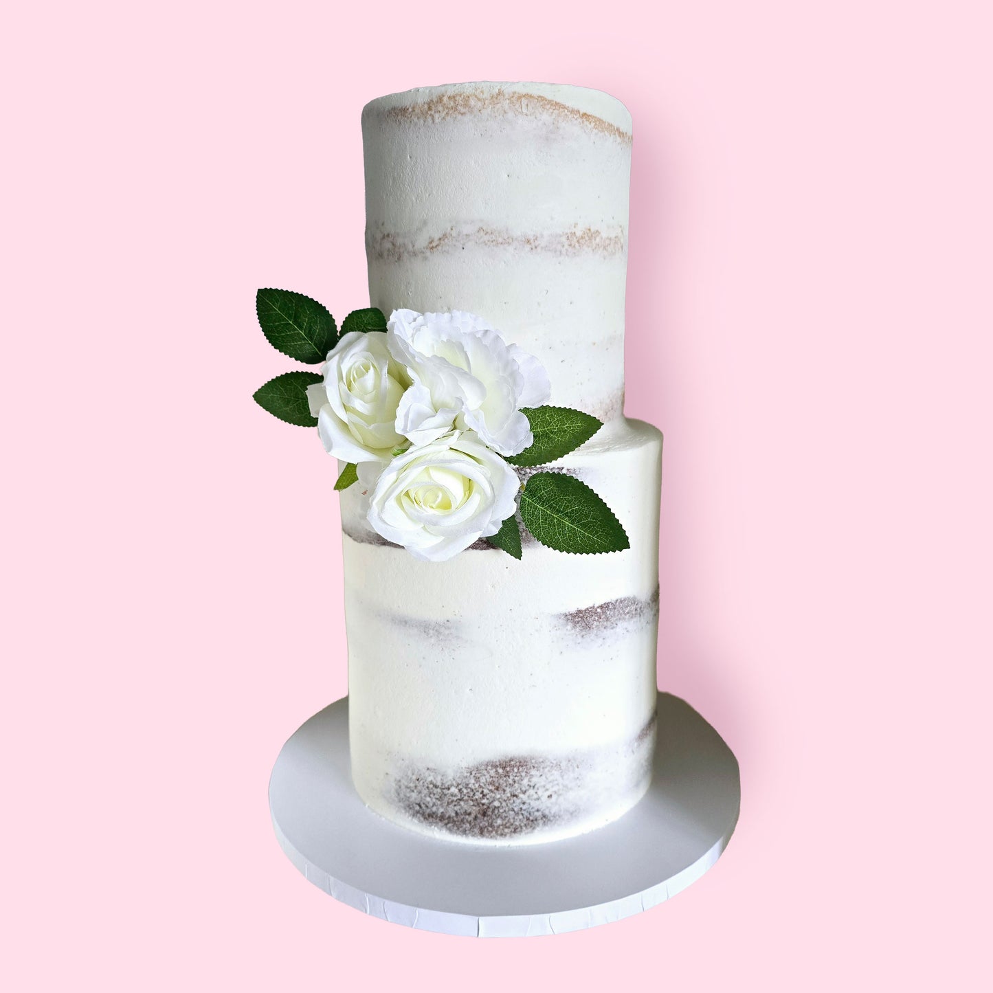Elegant semi-naked two-tier wedding cake with white buttercream finish and artificial white rose floral accents