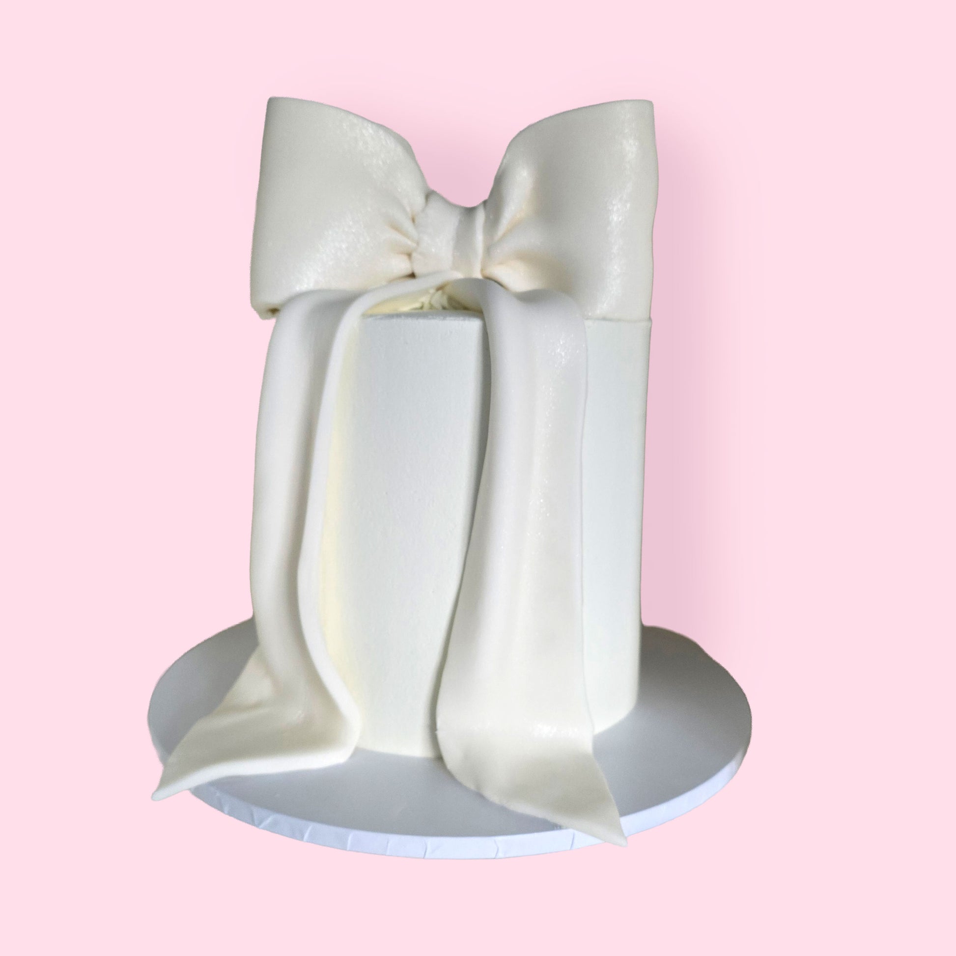 Minimalist white celebration cake with large fondant bow topper, perfect for weddings or luxury birthdays