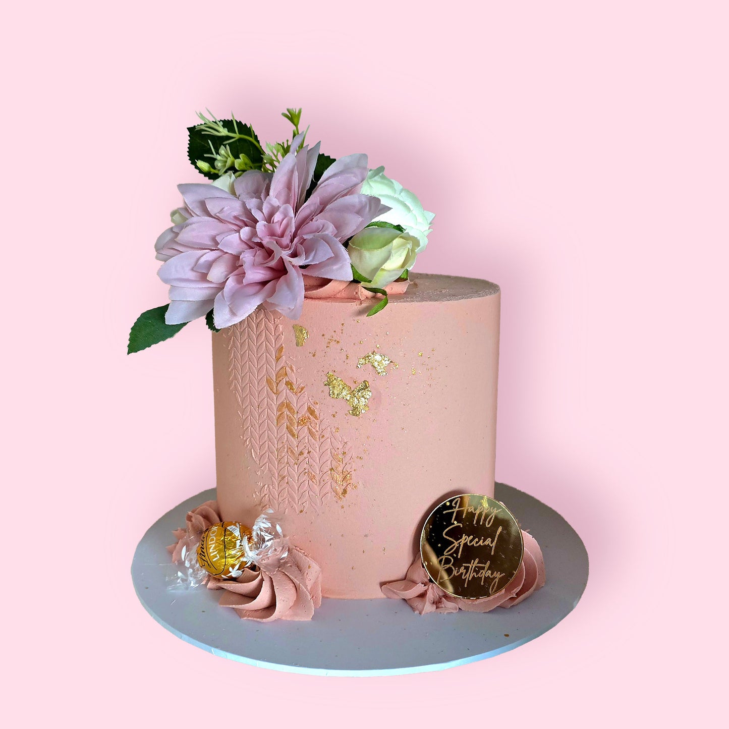 Elegant pink celebration cake with gold leaf, buttercream texture, and fresh floral toppers”