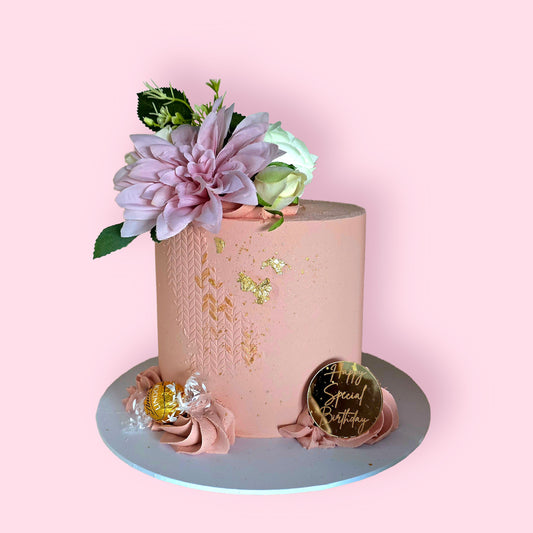 Elegant pink celebration cake with gold leaf, buttercream texture, and fresh floral toppers”