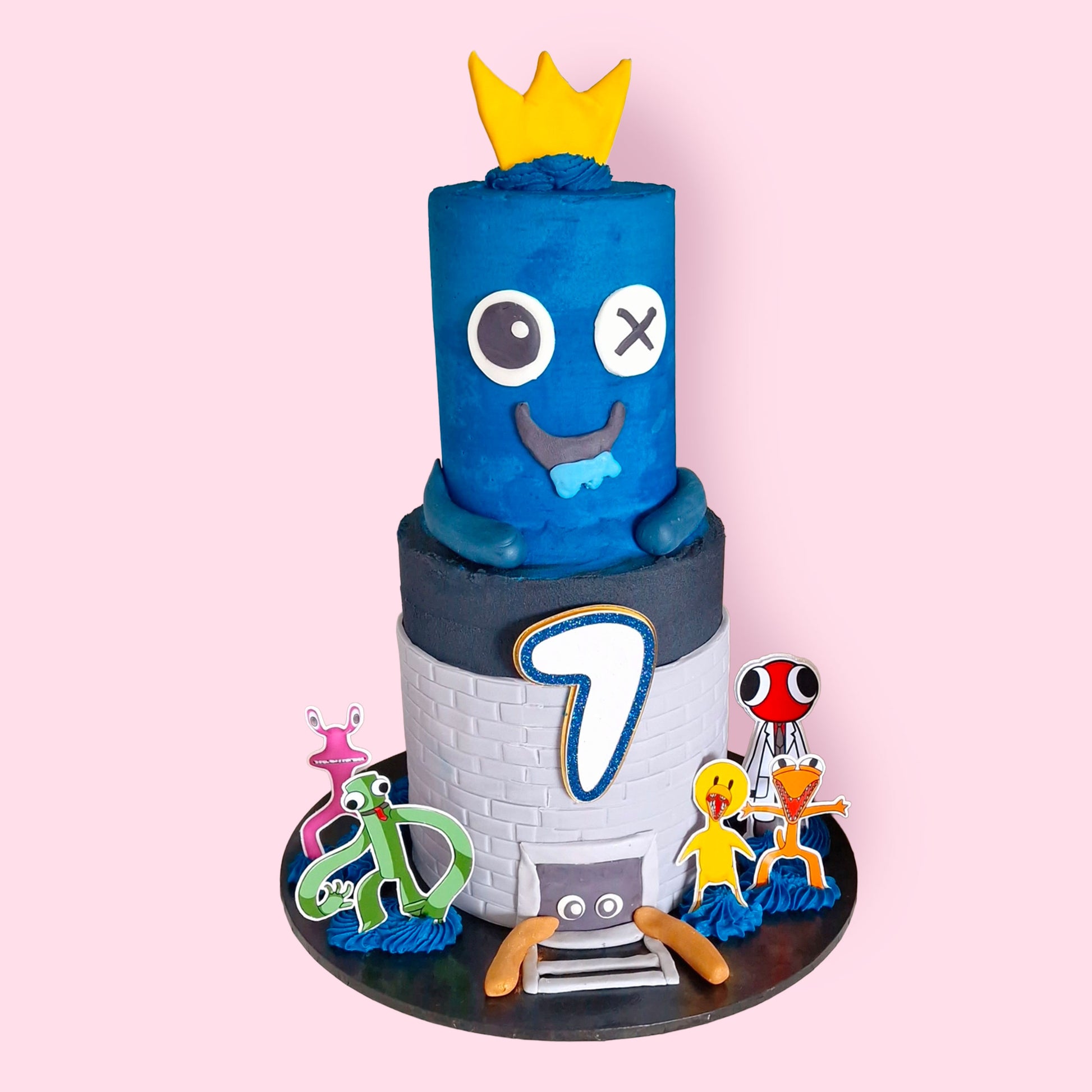 Blue character-themed two-tier birthday cake with crown topper and age number 7, featuring colorful cartoon figures